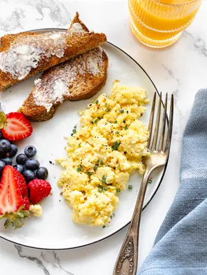 cottage cheese scrambled eggs paired with toast, juice and a side of fruit for breakfast