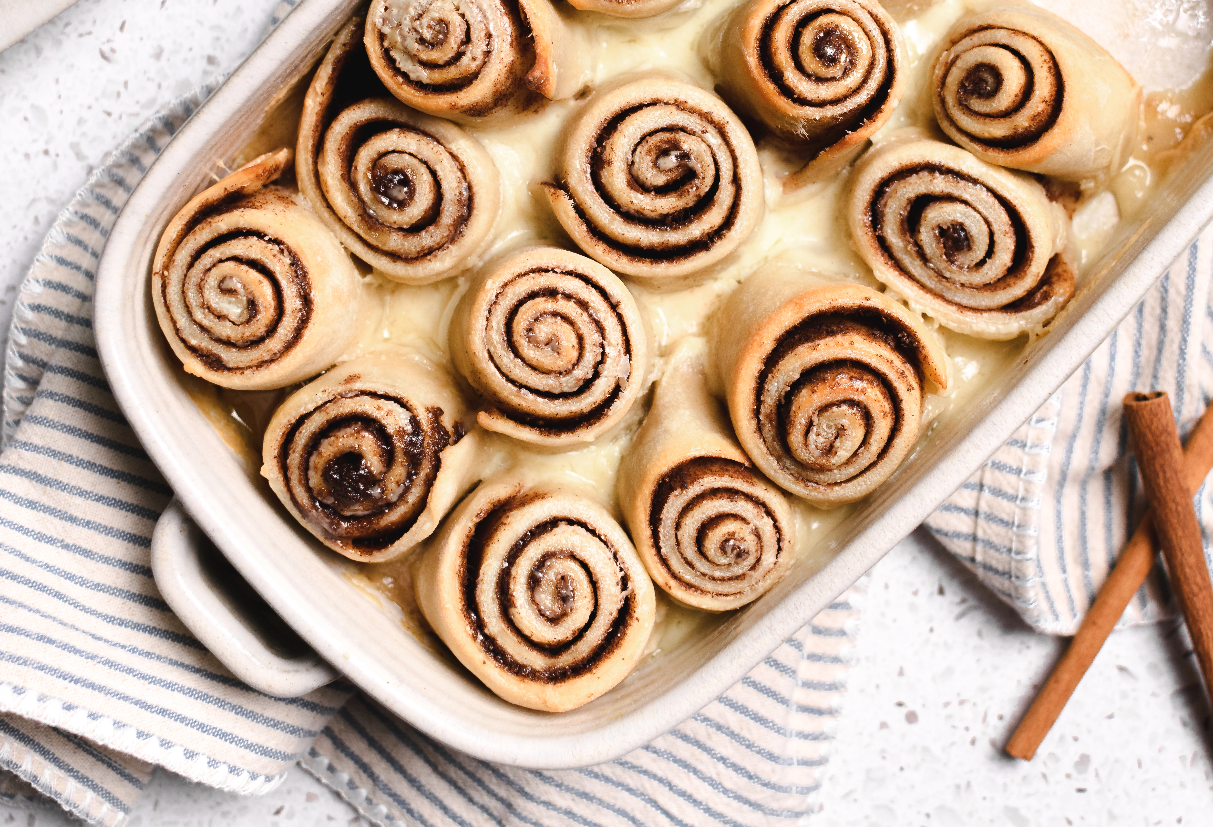 Greek Yogurt Chai Cinnamon Rolls covered in heavy cream in a baking dish.