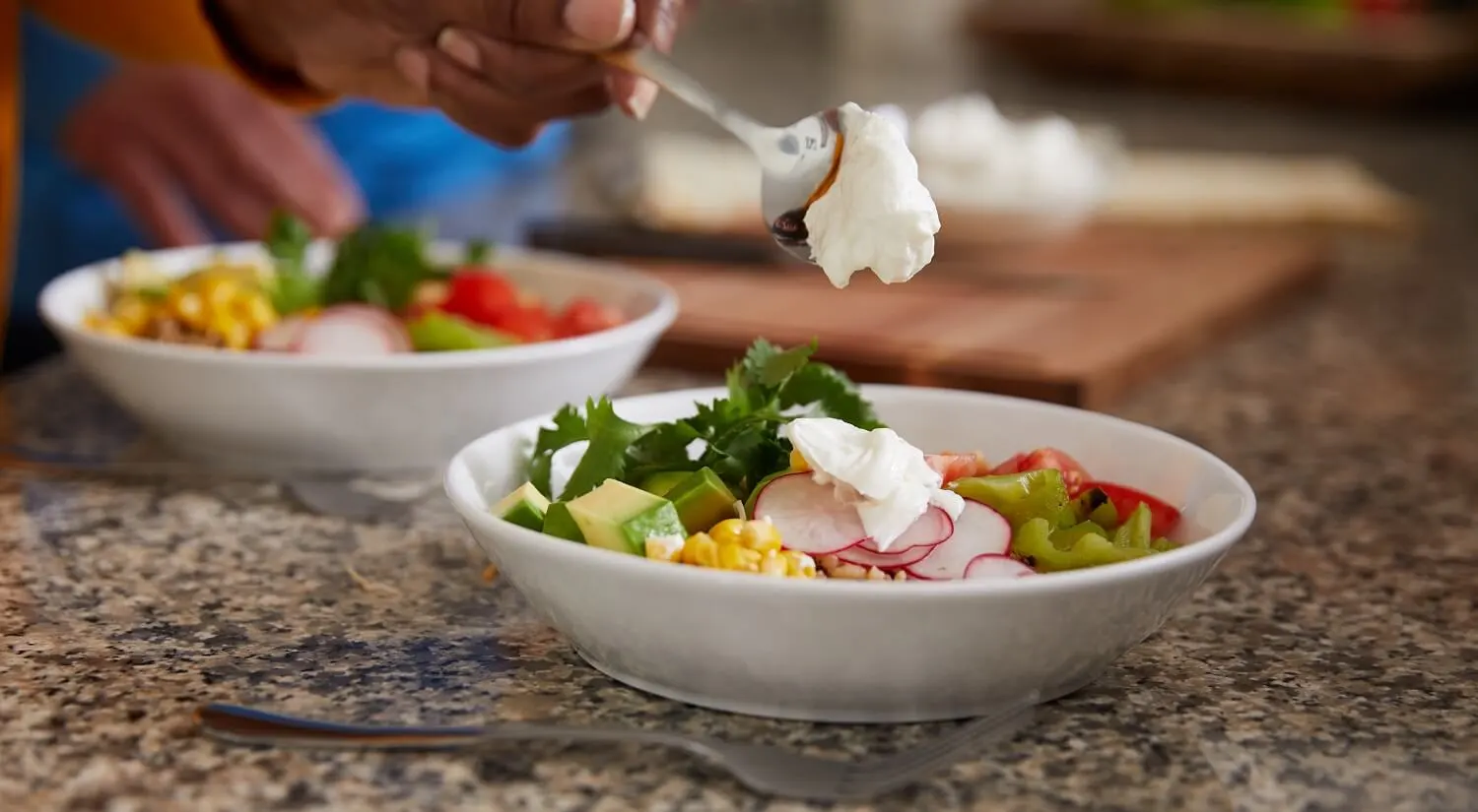 A bowl of vegetables dressed with Greek yogurt next to another bowl and a fork.