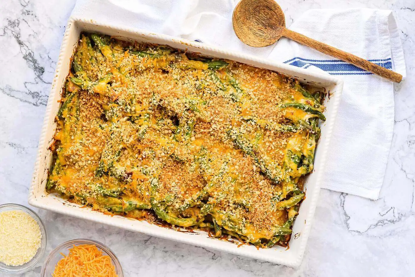 A rectangular baking dish containing green beans in a cream sauce topped with melted cheddar cheese and breadcrumbs.