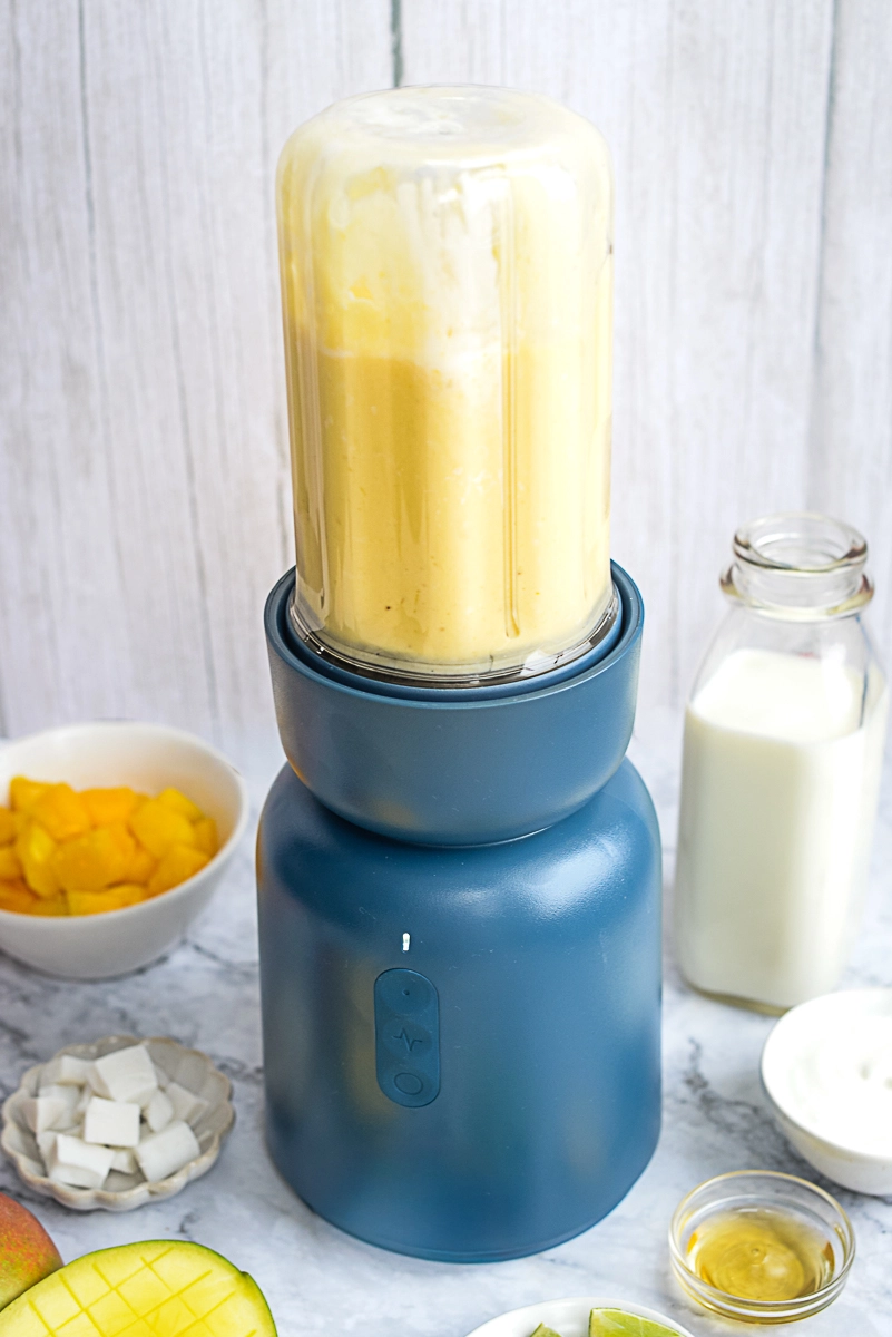 Tropical smoothie blended in blender, with ingredients in bowls beside blender