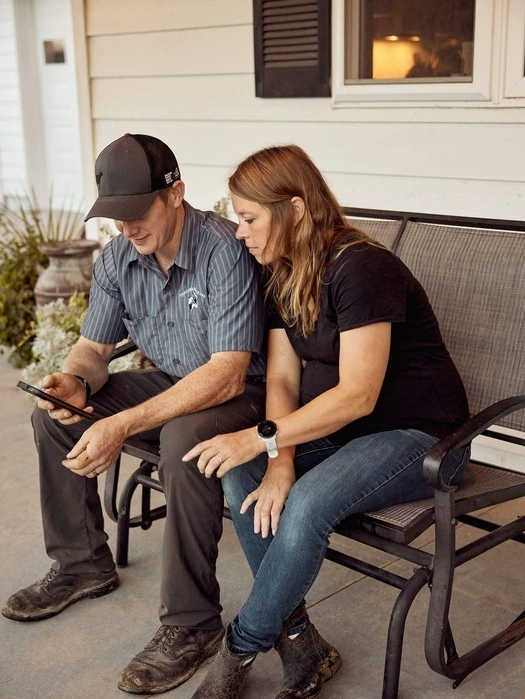 Two dairy farmers reviewing a tablet while seated outside